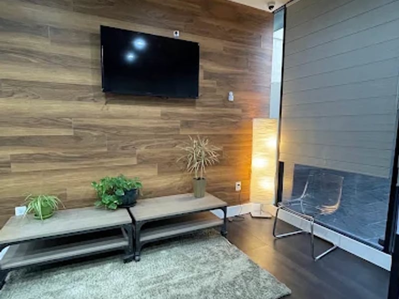 A comfortable consultation lounge at Sarubin Family Dental, with a wood accent wall, wall-mounted TV, plants, and modern seating